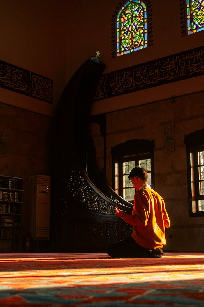 A man in contemplative prayer inside a mosque with colorful stained glass windows.
